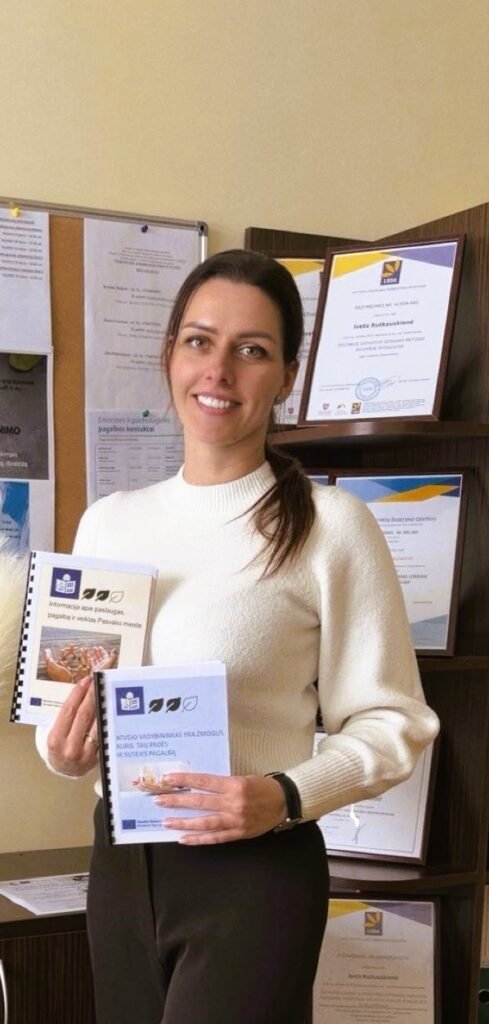 Nuotraukoje matoma moteris, stovinti biuro patalpoje. Ji atsisukusi į kamerą, šypsosi, atrodo rami ir draugiška. Moteris vilki šviesų, ilgomis rankovėmis megztinį, jos tamsūs plaukai surišti atgal.
Rankose ji laiko dvi nedideles lengvai suprantamos kalbos metodines knygeles su spalvotais viršeliais – viena mėlyna, kita gelsva. Ant viršelių matyti iliustracijos ir tekstas.
Už moters nugaros – lentyna su įrėmintais dokumentais, diplomais ir sertifikatais. Taip pat matosi skelbimų lenta su prisegtais lapais. 
