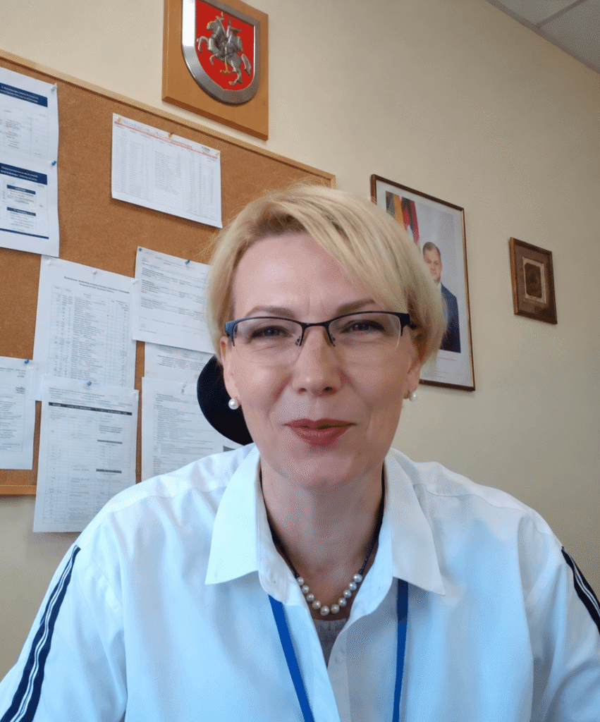 Nuotolinės diskusijos apie bendruomeninių paslaugų plėtrą dalyvė – šviesiaplaukė moteris su akiniais, sėdinti darbo kabinete priešais kamerą